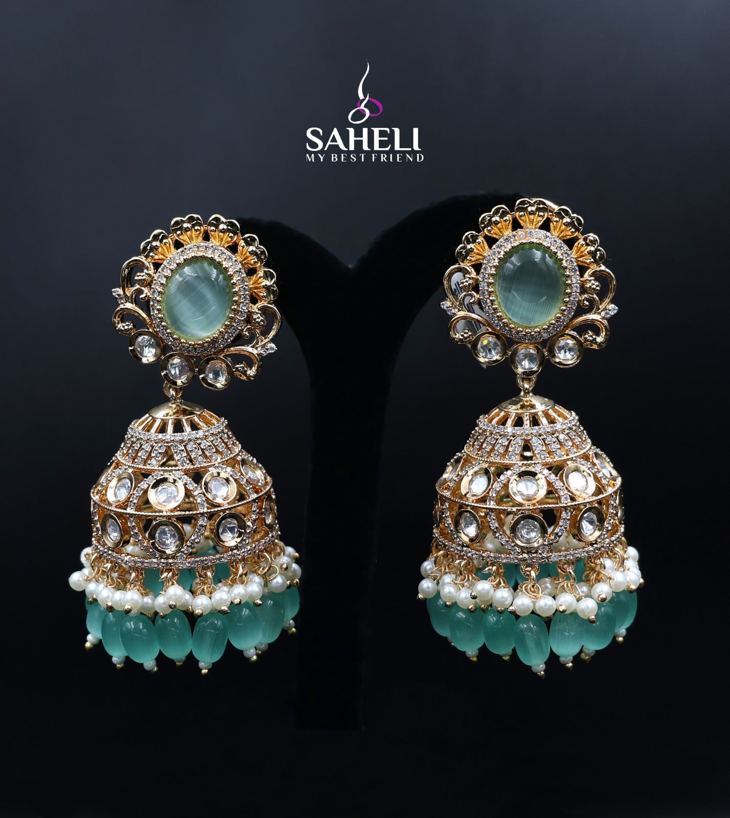 Ornate earrings with turquoise stones and pearl accents on a dark background, featuring the brand 'Saheli'.