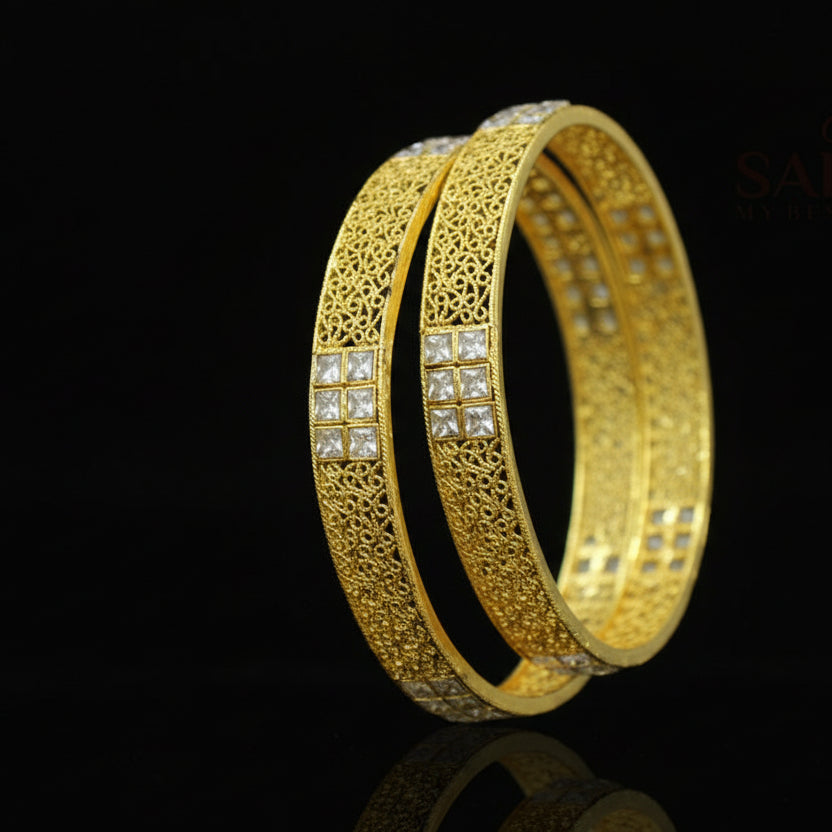 Gold bangles with intricate designs on a dark background, featuring the brand 'Saheli'.
