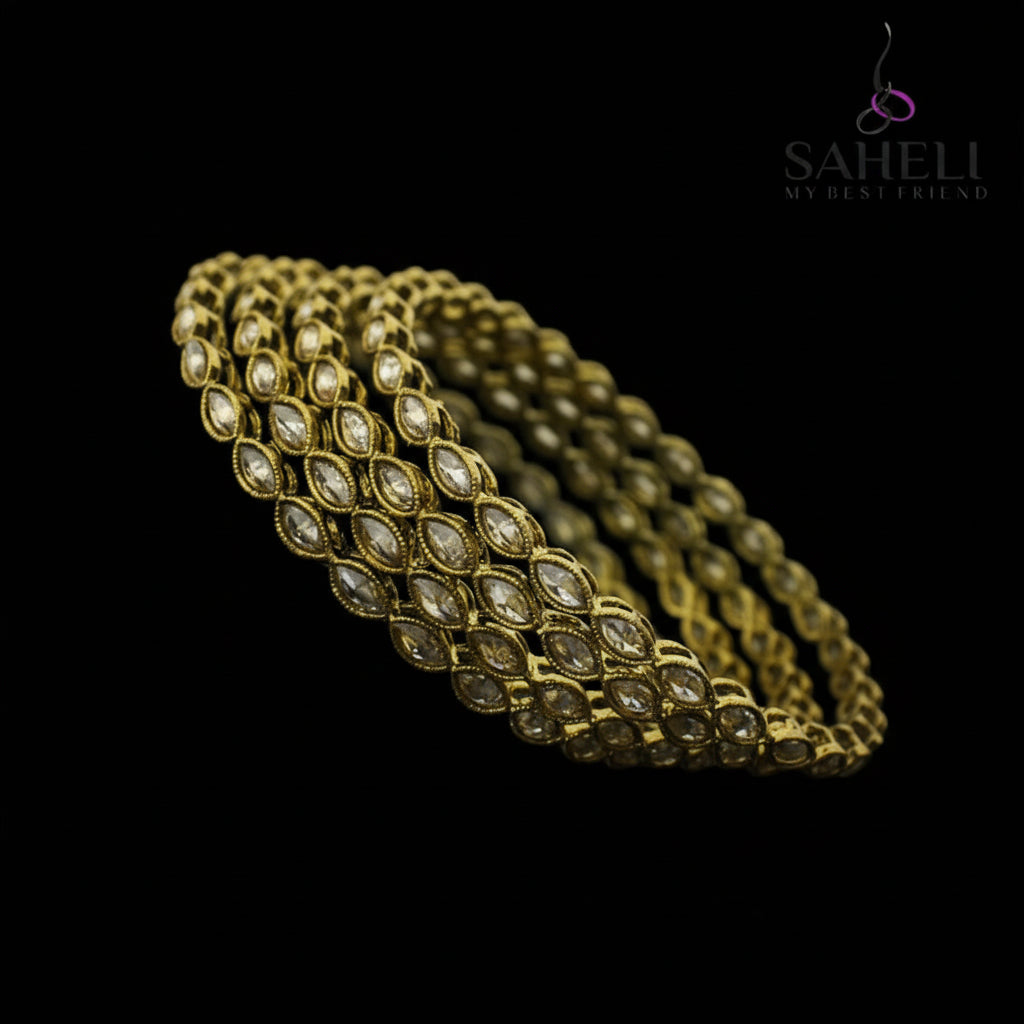 Gold bracelet with clear stones on a black stand, branded 'Saheli'.