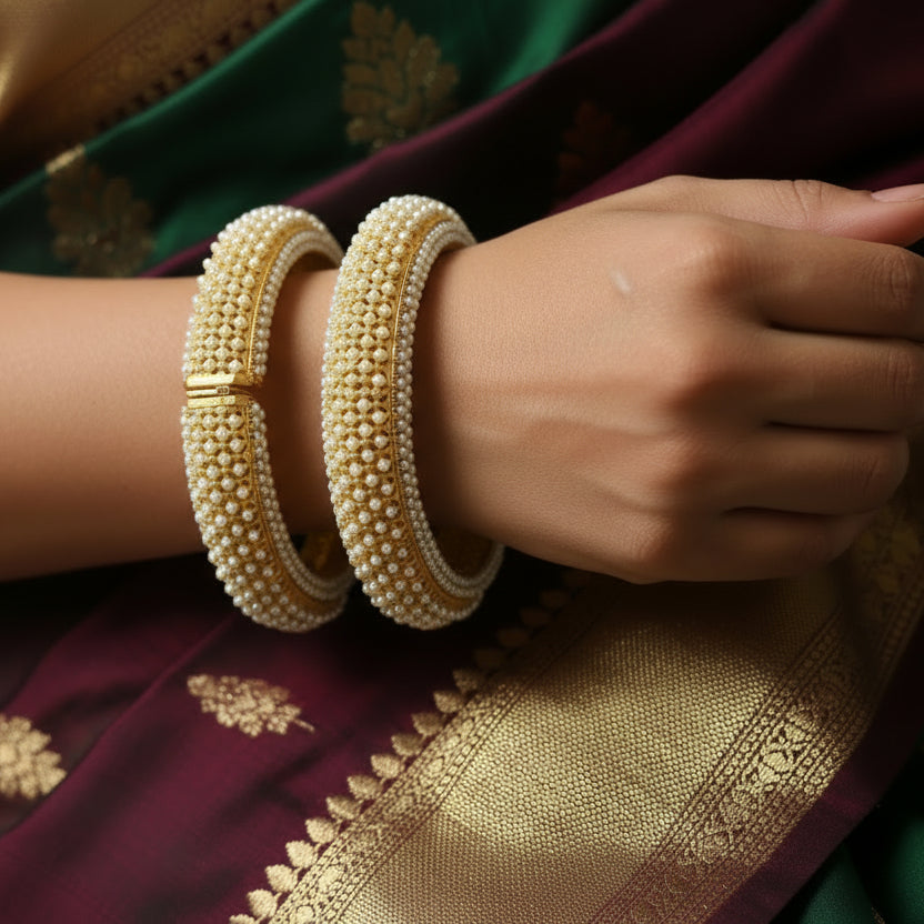 Gold bangles with pearl detailing on a gray background, featuring the brand 'SAHELI'.