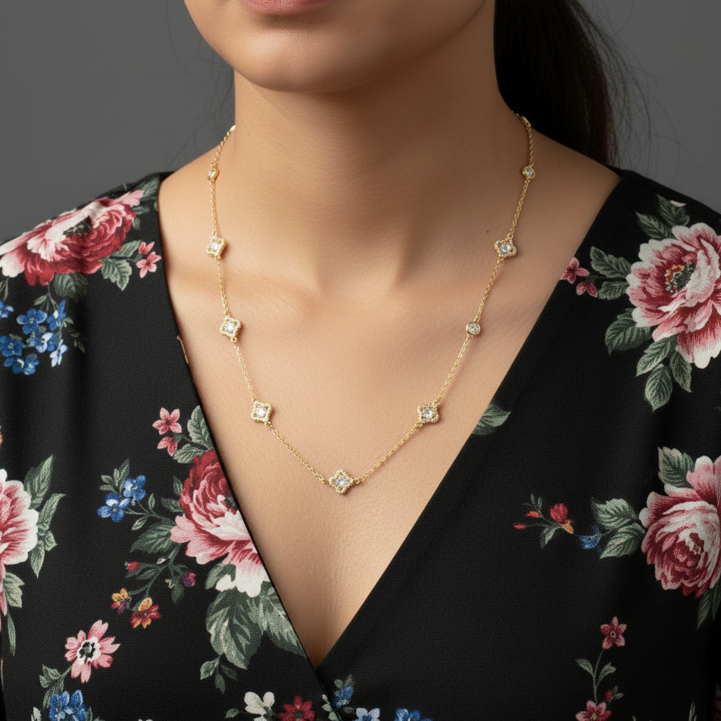 Gold necklace with embedded stones on a black background, featuring the brand 'Saheli'.