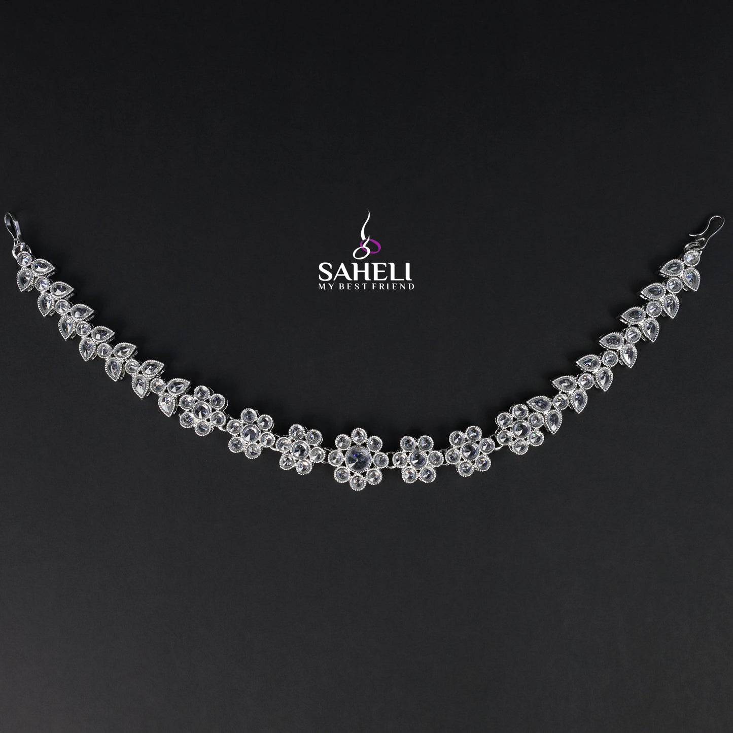 Silver necklace with floral design on a black background, featuring the brand 'Saheli'.