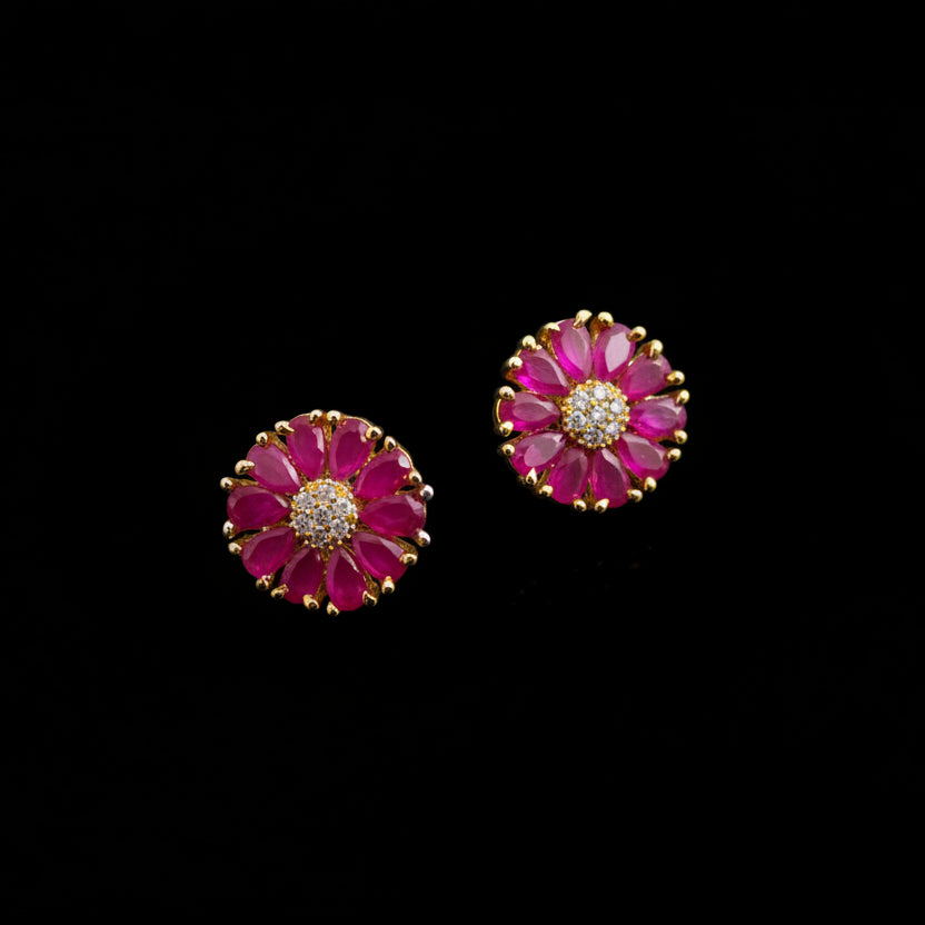 Pair of pink flower-shaped earrings with gold accents on a gray background with 'SAHELI' branding.