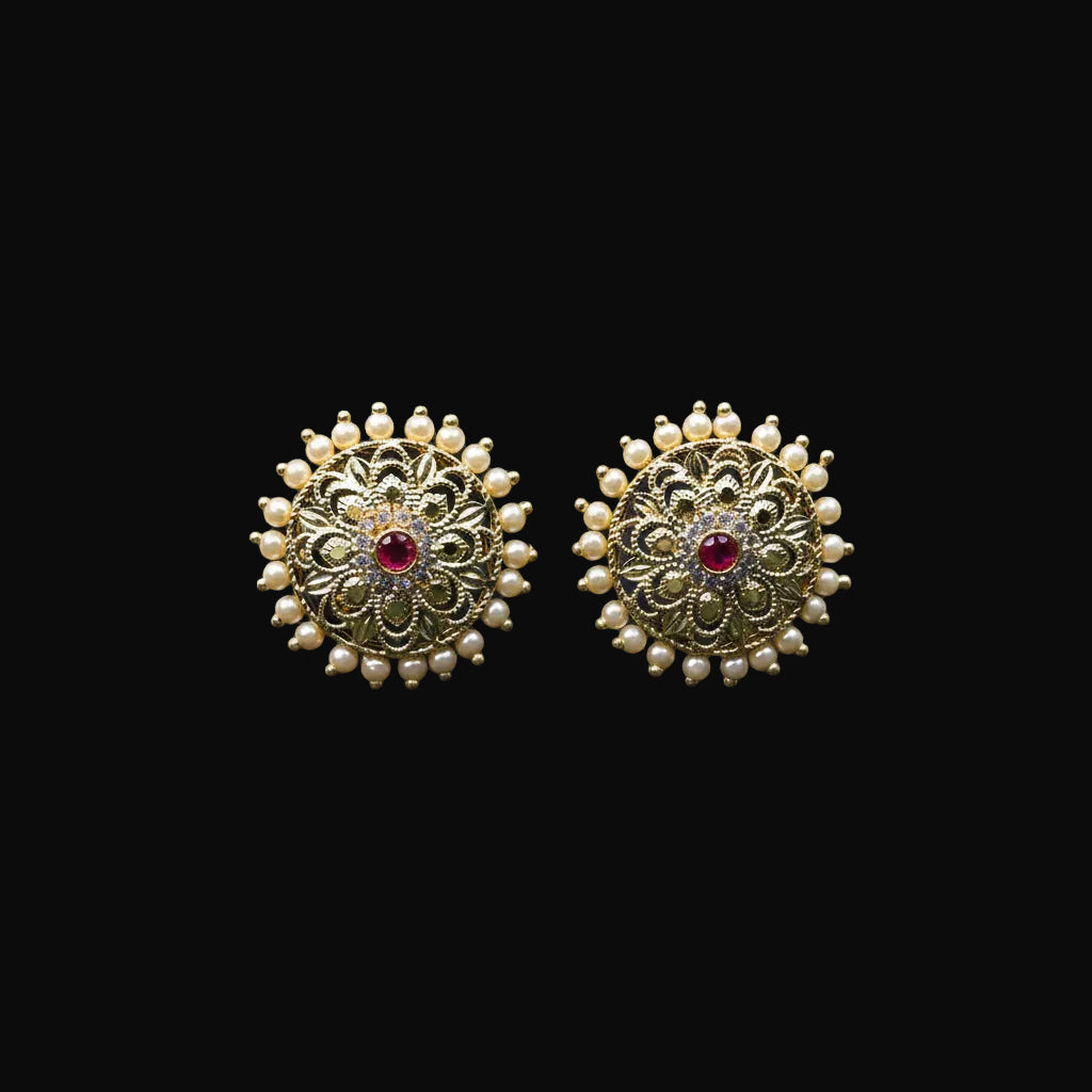 Gold earrings with red gemstones on a black stand, featuring the brand 'SAHELI'.
