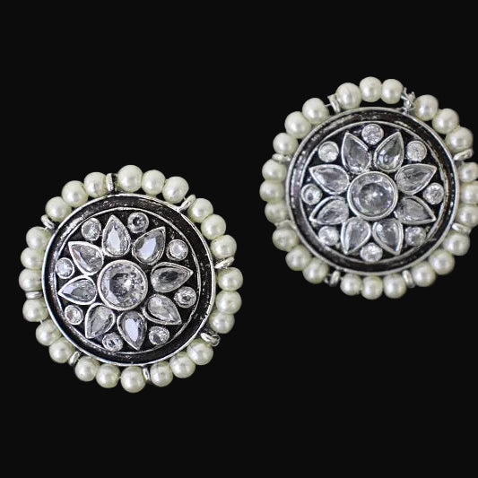 Pair of decorative earrings with floral designs and pearl accents on a dark background