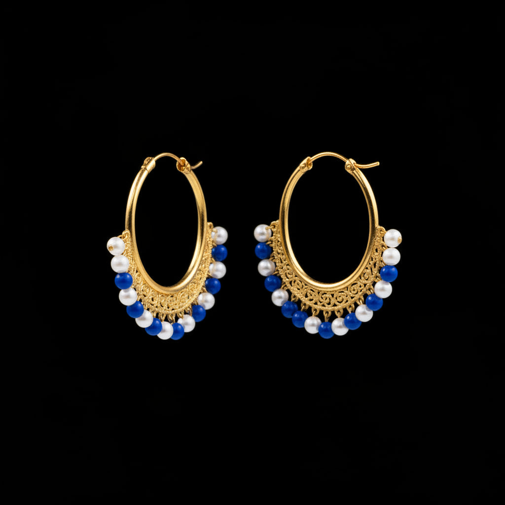 A pair of gold hoop earrings with dangling pearl-like bead clusters, photographed on a gray textured surface with a small white price tag attached to one earring.