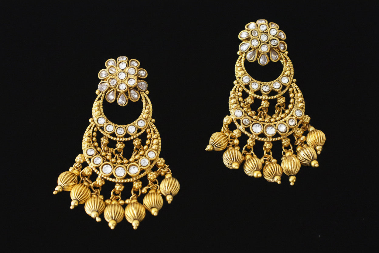 Gold earrings with intricate designs on a dark background, branded 'Saheli'.