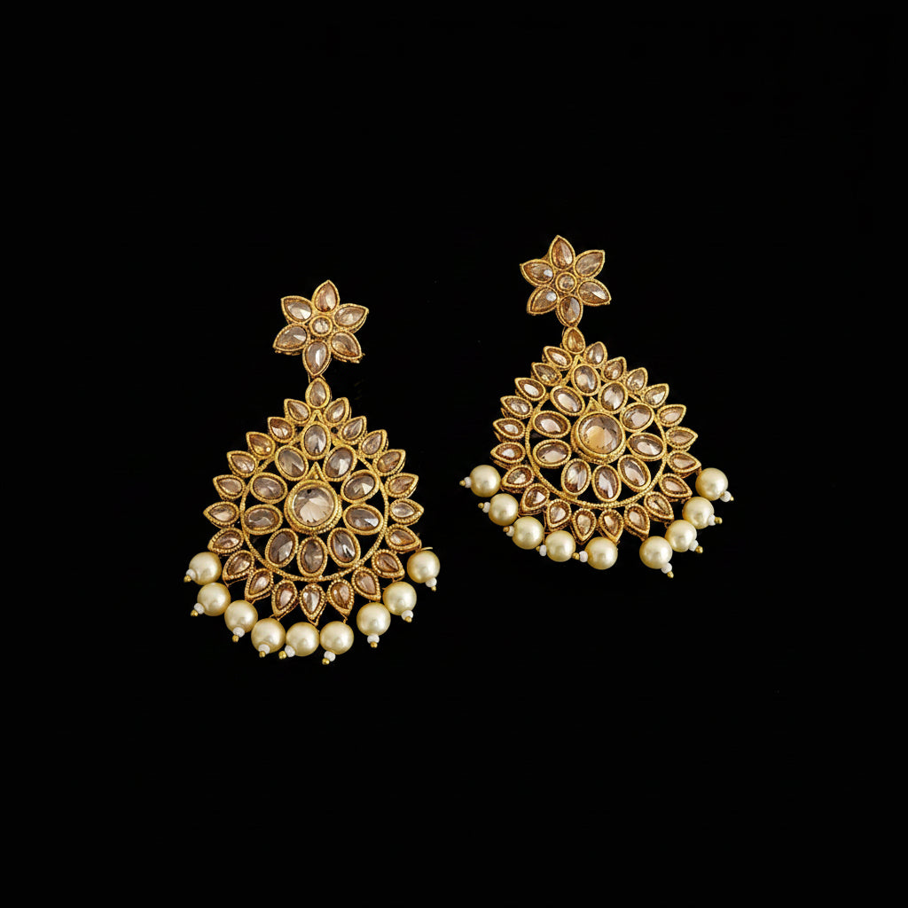 A pair of gold-toned Indian jhumka earrings with clear stones and white pearl bead drops, displayed on a dark reflective surface with the brand name 'SAHELI MY BEST FRIEND' at the top.