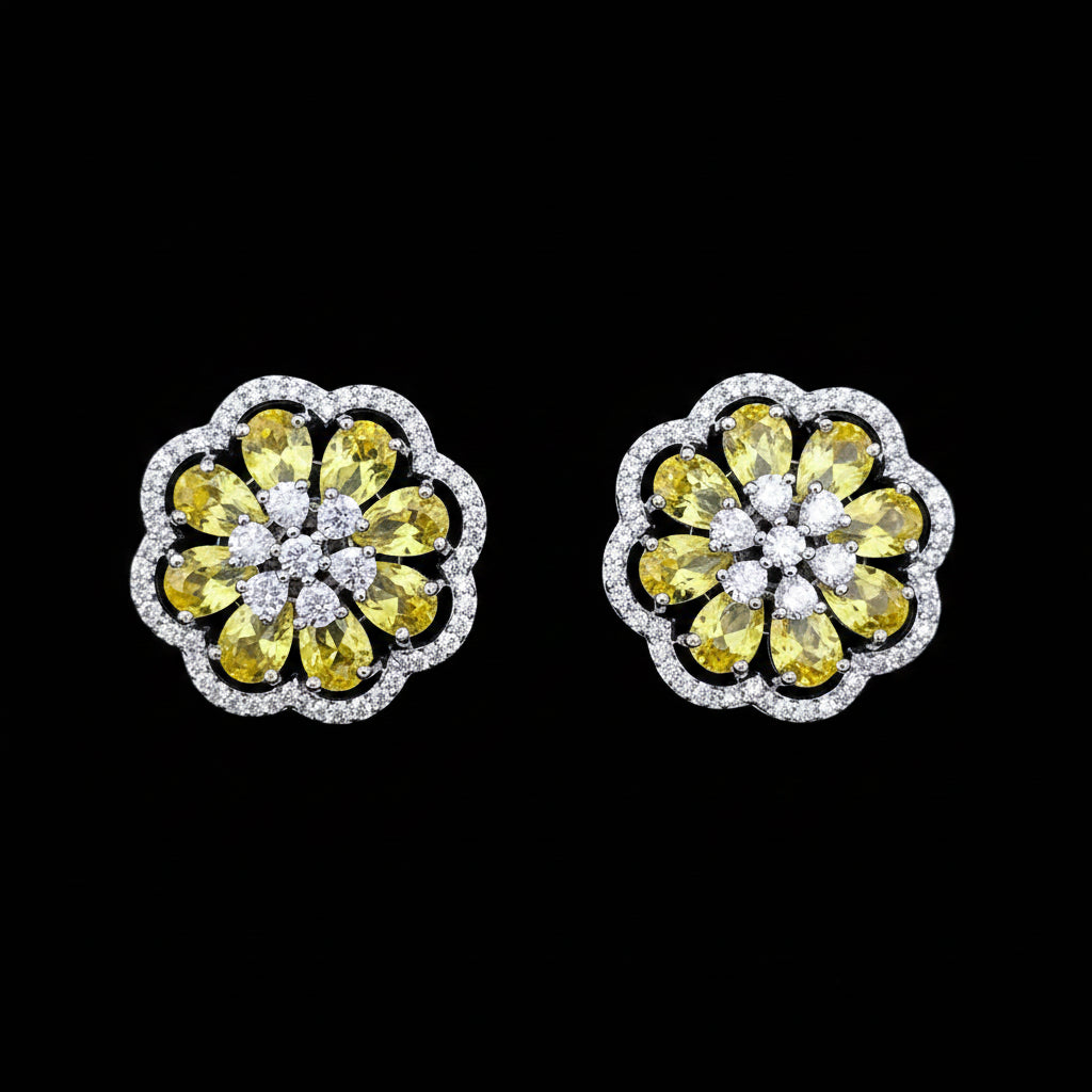 A pair of round floral stud earrings featuring yellow gemstones in a flower pattern with a silver-colored halo border, set against a solid blue background.