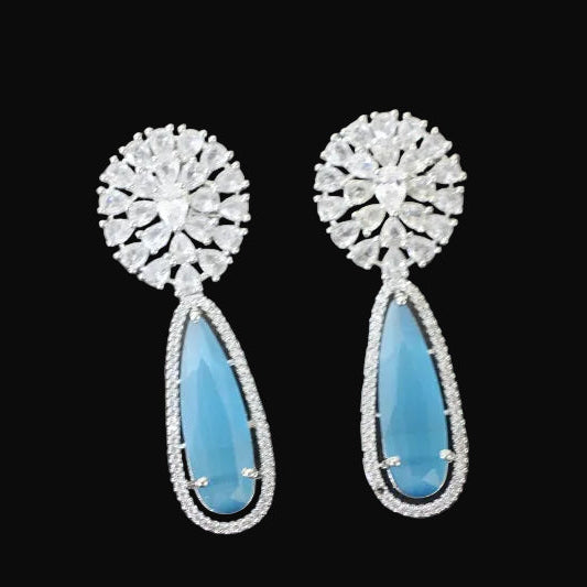 Pair of earrings with blue teardrop stones and silver floral tops on a gray surface.