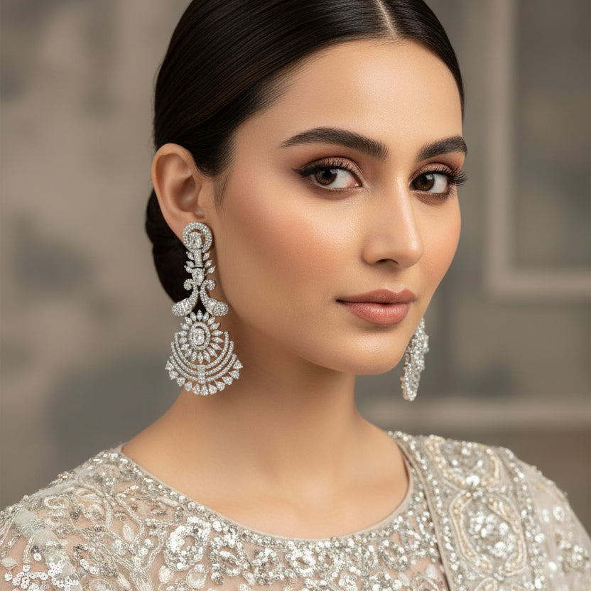 Pair of silver earrings with intricate designs on a dark background, branded 'Saheli'.