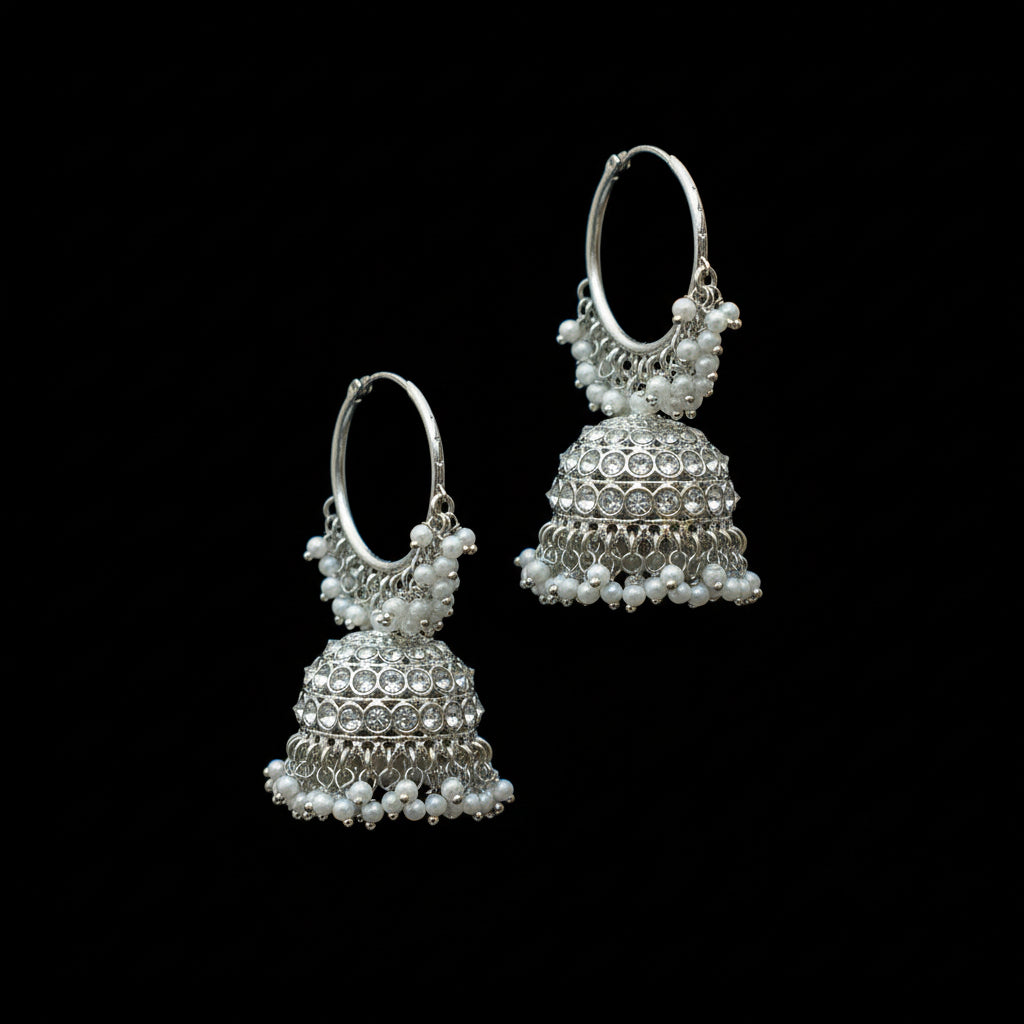 Silver jhumka earrings with pearls on a black stand against a gray background, branded 'Saheli'.