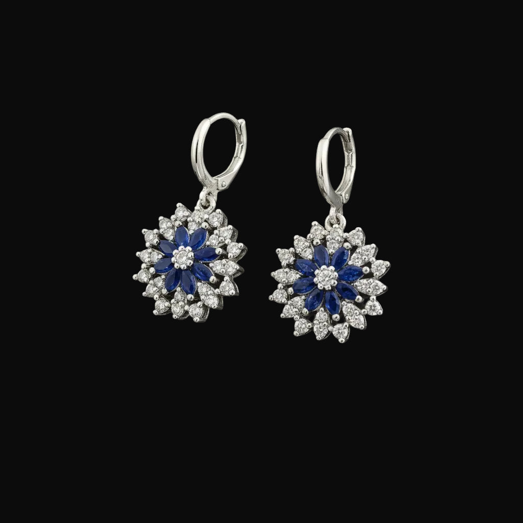 Pair of silver earrings with blue and white stones on a gray background, branded 'Saheli'.