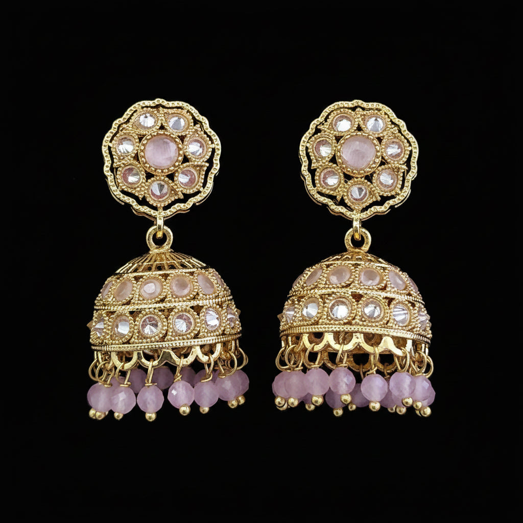A pair of ornate gold-toned jhumka earrings embellished with clear stones and pink beads, displayed on a solid dark pink background.