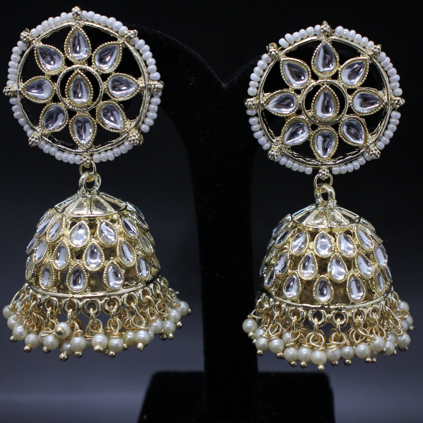Pair of gold and pearl jhumka earrings on a black stand.