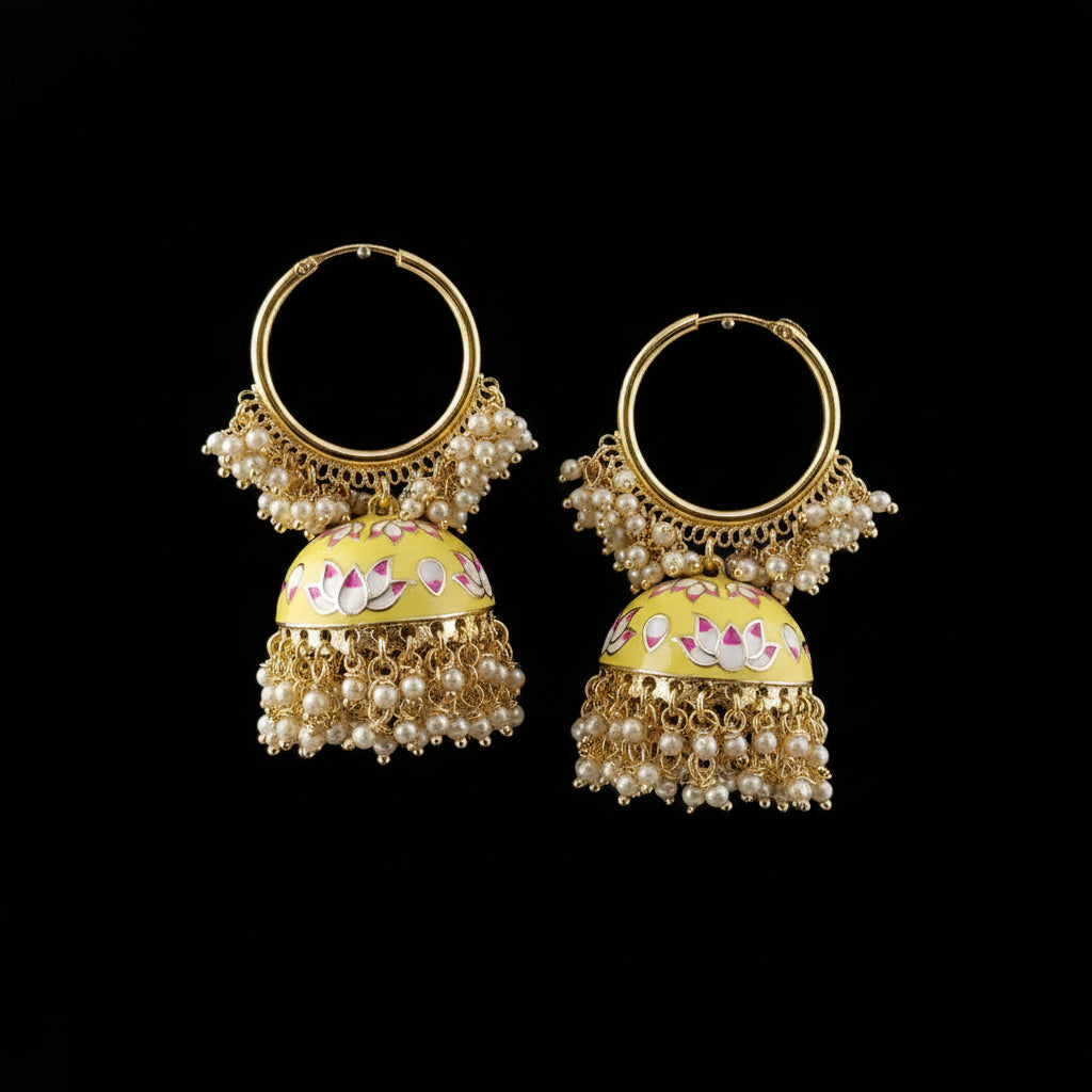 A pair of ornate gold-toned jhumka earrings with yellow enamel, pink floral details, and white pearl bead fringe, displayed on black stand forms against a gray background.