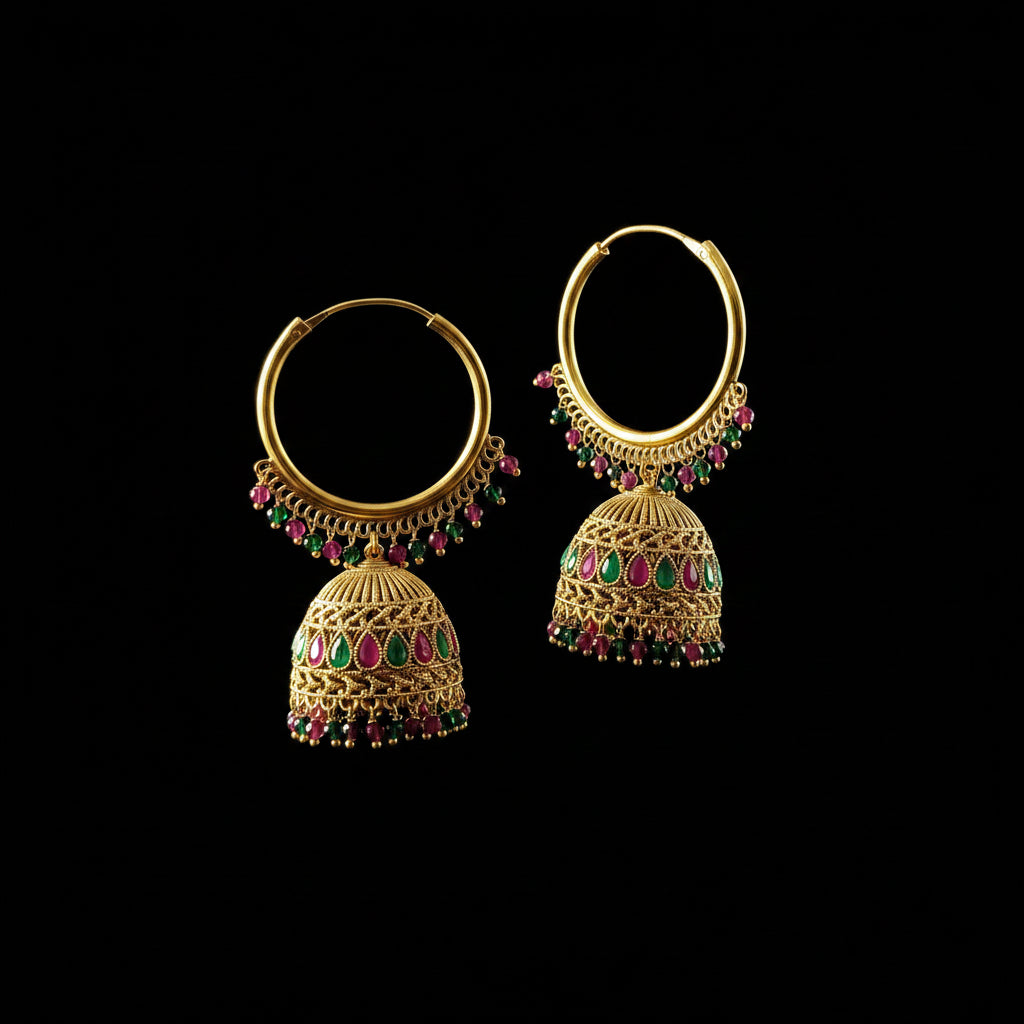 A pair of gold-toned hoop earrings with ornate filigree jhumka-style dangling bells, decorated with pink and green stone accents, displayed on a gray jewelry stand against a gray background.