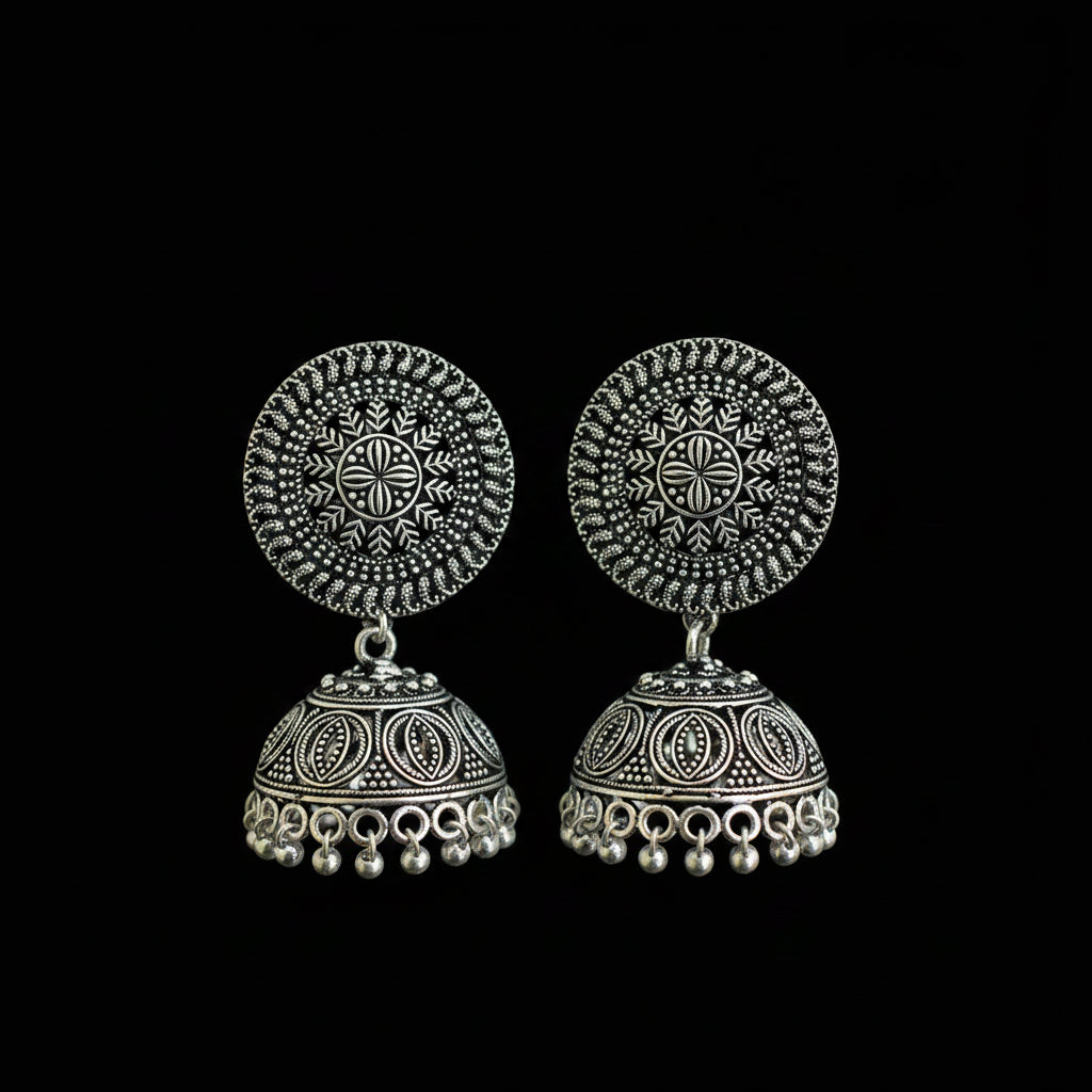 Pair of silver earrings on a green feather against a dark background