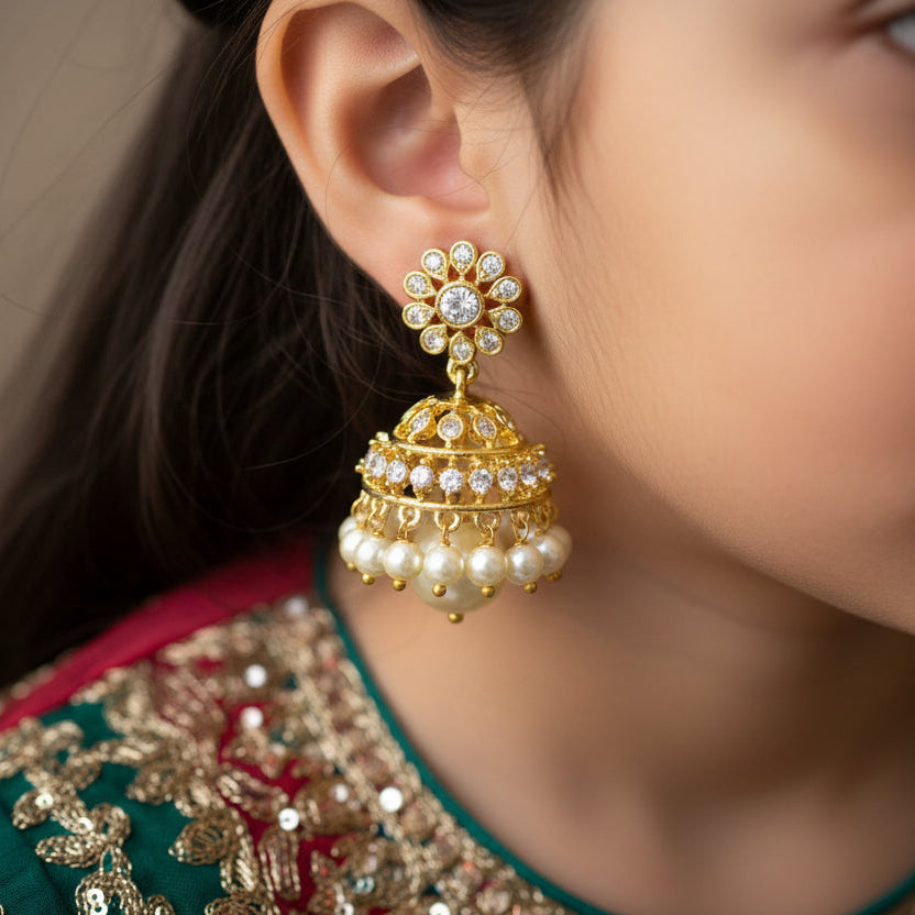Close-up of a person wearing gold and pearl earrings with a blurred background
