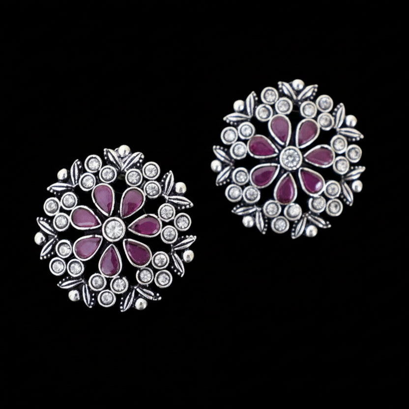 Pair of floral earrings with purple and clear stones on a gray background