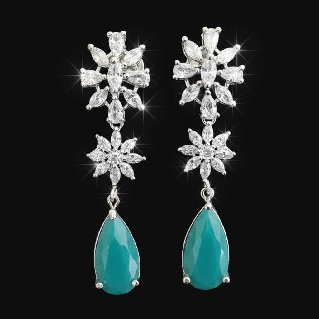 Pair of earrings with star-shaped top and teardrop-shaped bottom on a gray background, branded 'SAHELI'.
