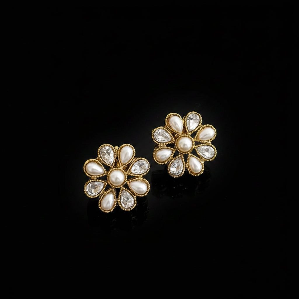 Pair of floral earrings with gold and pearl details on a dark background, featuring the brand 'Saheli'.