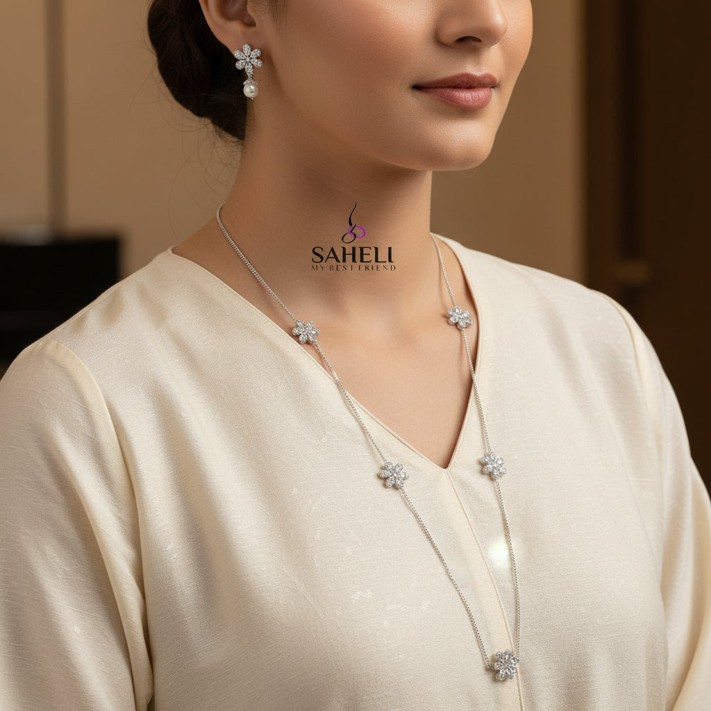 Silver necklace with floral pendants on a dark background, featuring the brand 'Saheli'.