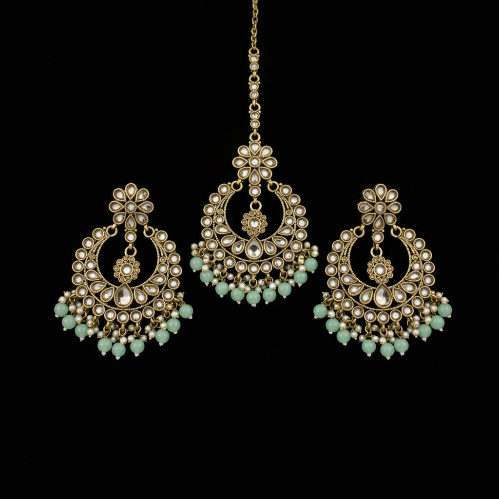 Ornate gold earrings with green stones on a dark background