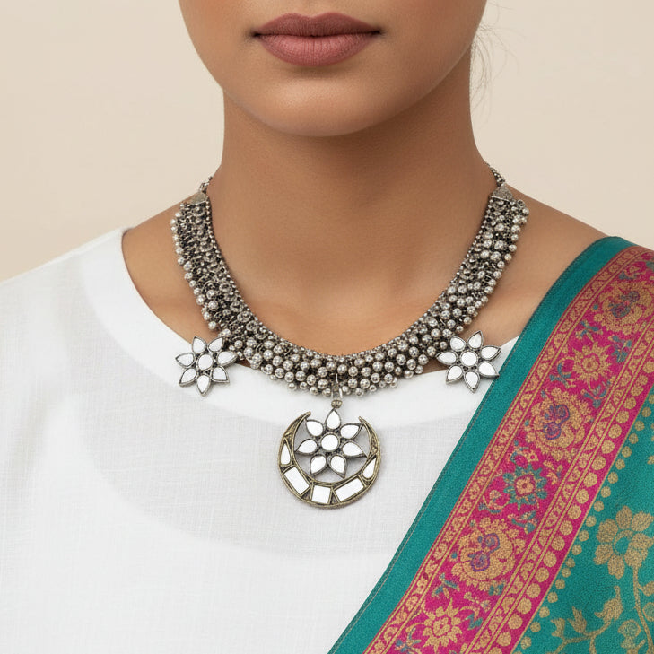 Silver necklace with floral pendants on a dark background, featuring the brand 'Saheli'.