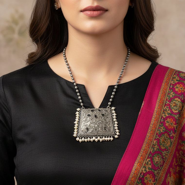 Silver necklace with intricate design and pearl accents on a white background, branded 'Saheli'.