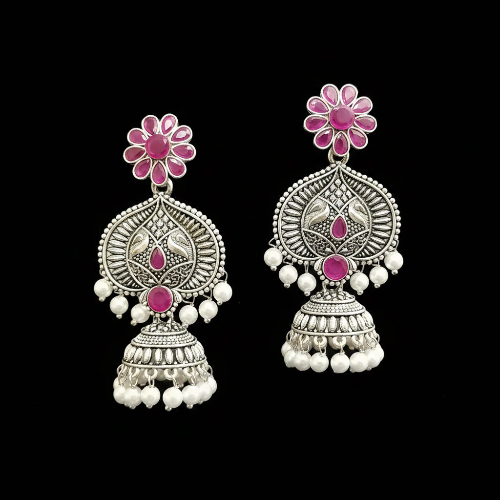 Ornate silver earrings with pink gemstones and pearl-like beads on a gray stand.