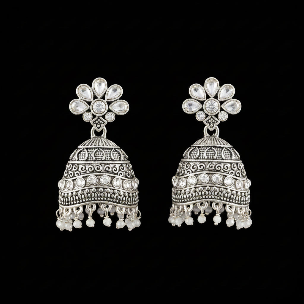 A pair of silver-toned Indian jhumka earrings with blue stone accents, displayed on a gray velvet jewelry stand against a light gray background.