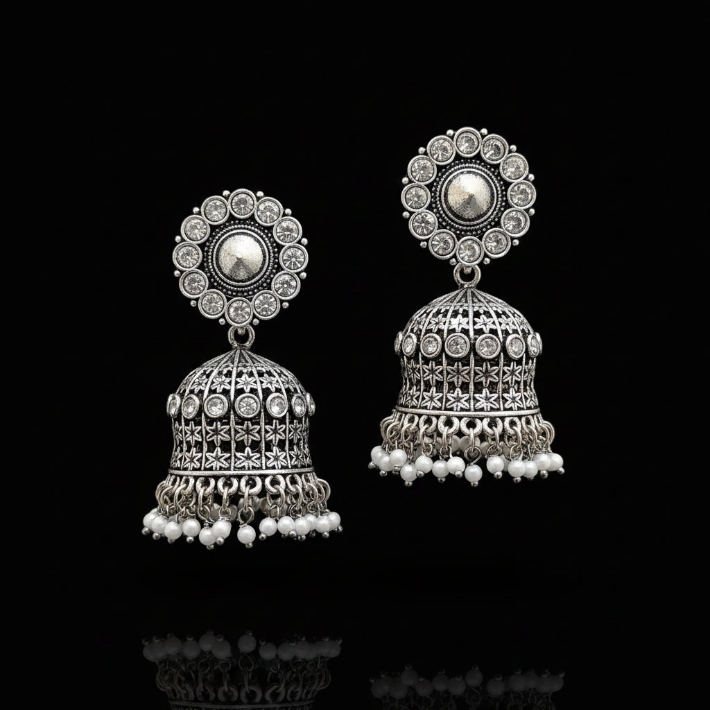 Pair of silver jhumka earrings with white beads on a gray stand.