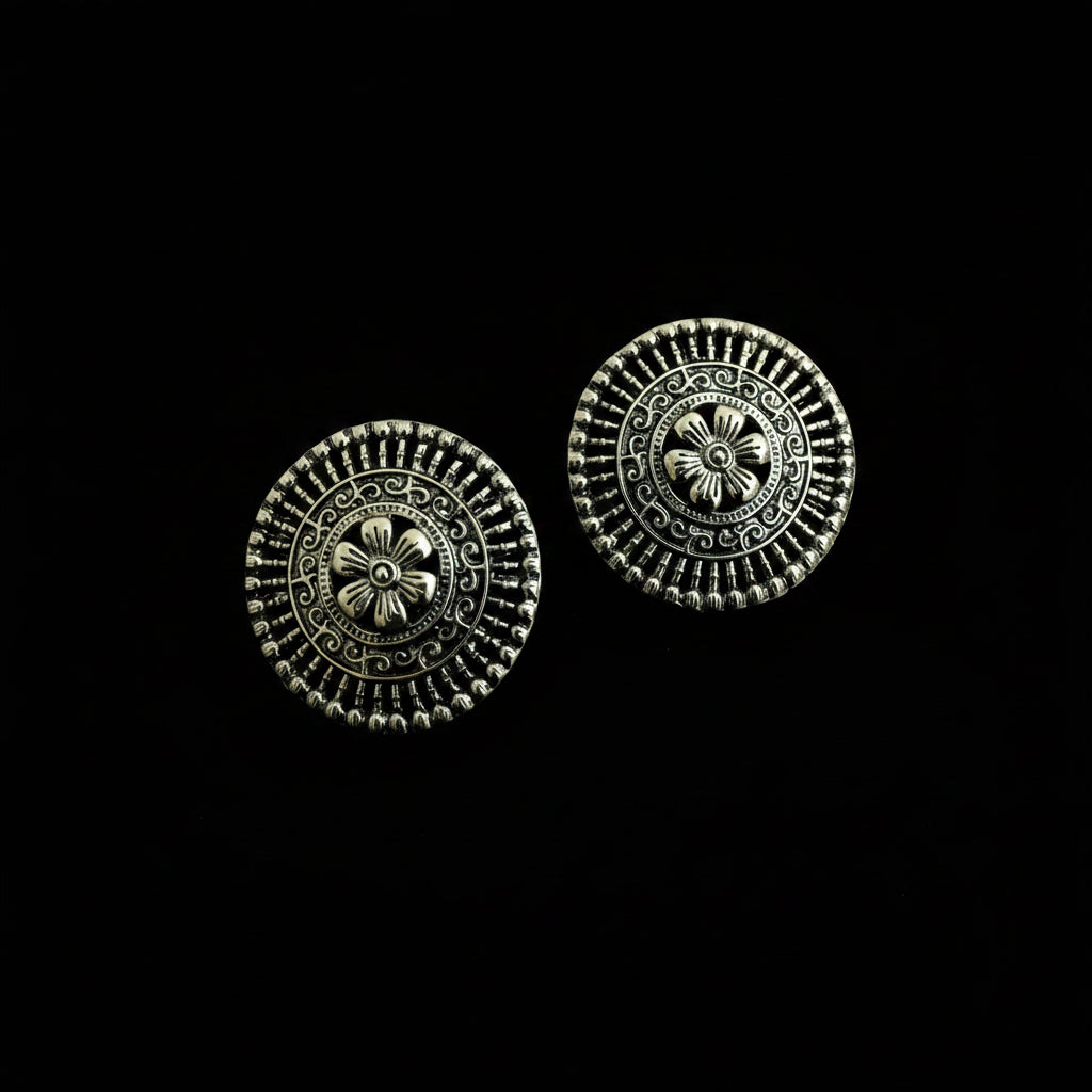 A pair of round silver-toned metal buttons with intricate floral and geometric filigree detailing, displayed on a dark reflective surface.