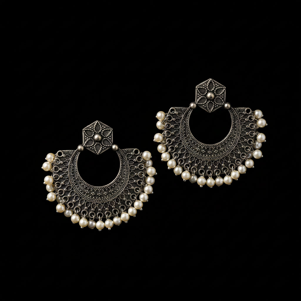 A pair of large silver-toned traditional Indian earrings with intricate filigree work, floral stud tops, and rows of small white faux pearls, displayed on a white background with a 'SAHeli My Best Friend' watermark at the top.