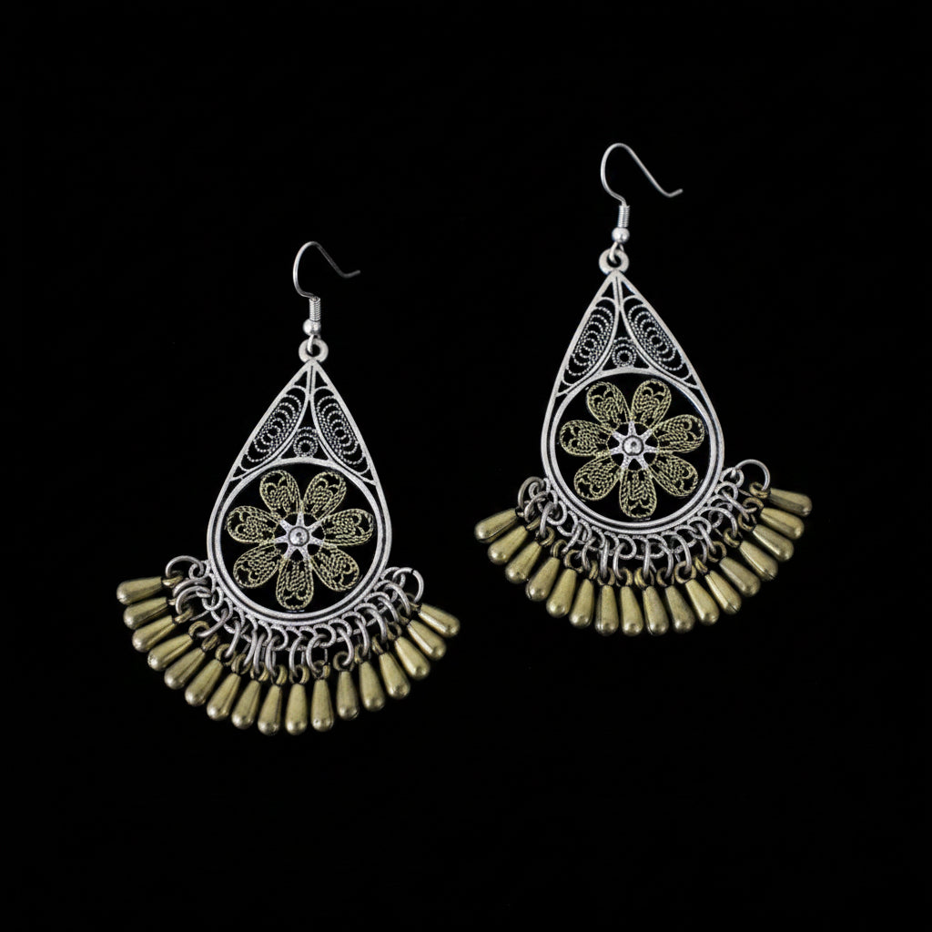 A pair of traditional Indian filigree dangle earrings with silver-tone metalwork, gold-tone floral centers, and dangling bell-shaped beads, displayed on a dark reflective surface with the SAHELI brand logo at the top.
