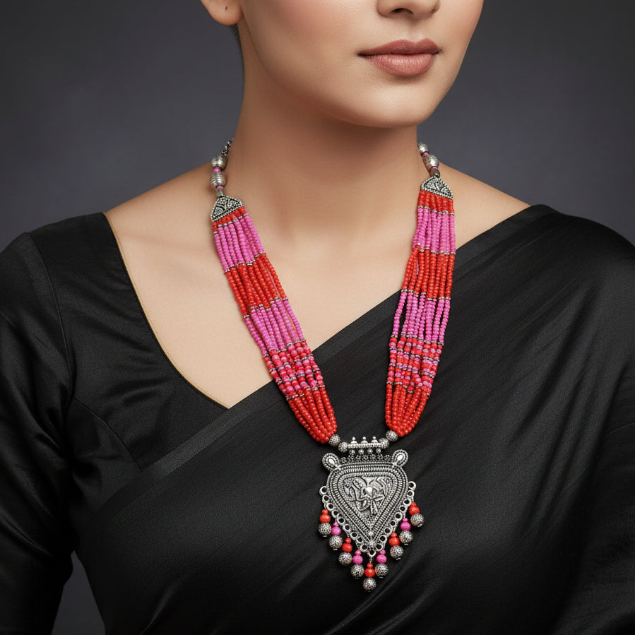 Colorful beaded necklace with silver pendant on a gray background, featuring the brand 'SAHELI'.