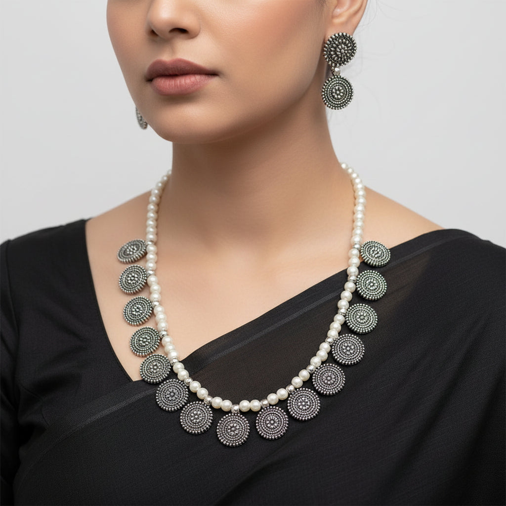 Pearl necklace with black circular pendants and matching earrings on a white background, branded 'Saheli'.
