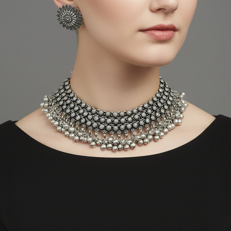 Silver necklace and earrings set on a reflective surface with 'Saheli' branding.