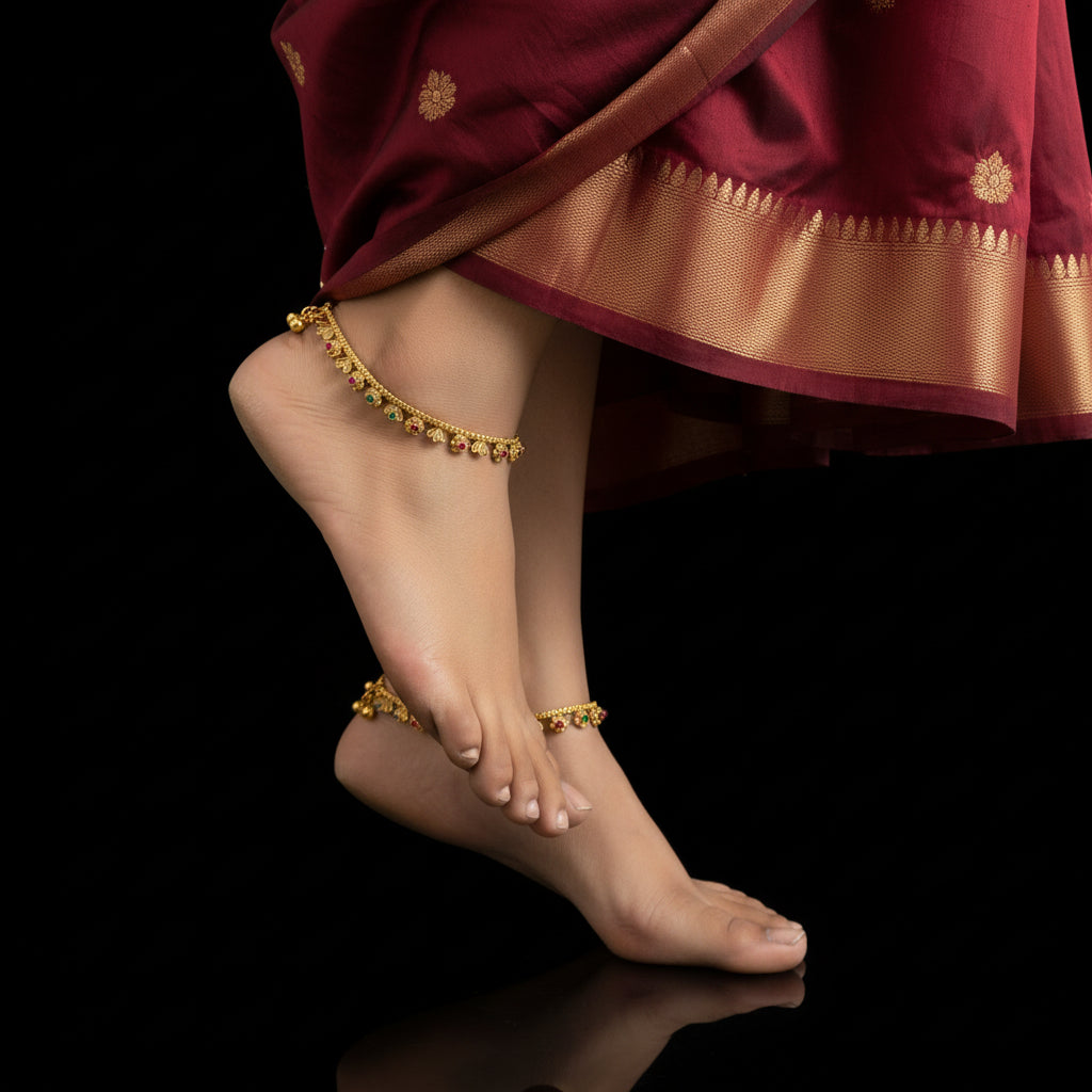 Feet with gold anklets wearing a maroon and gold traditional outfit on a black background