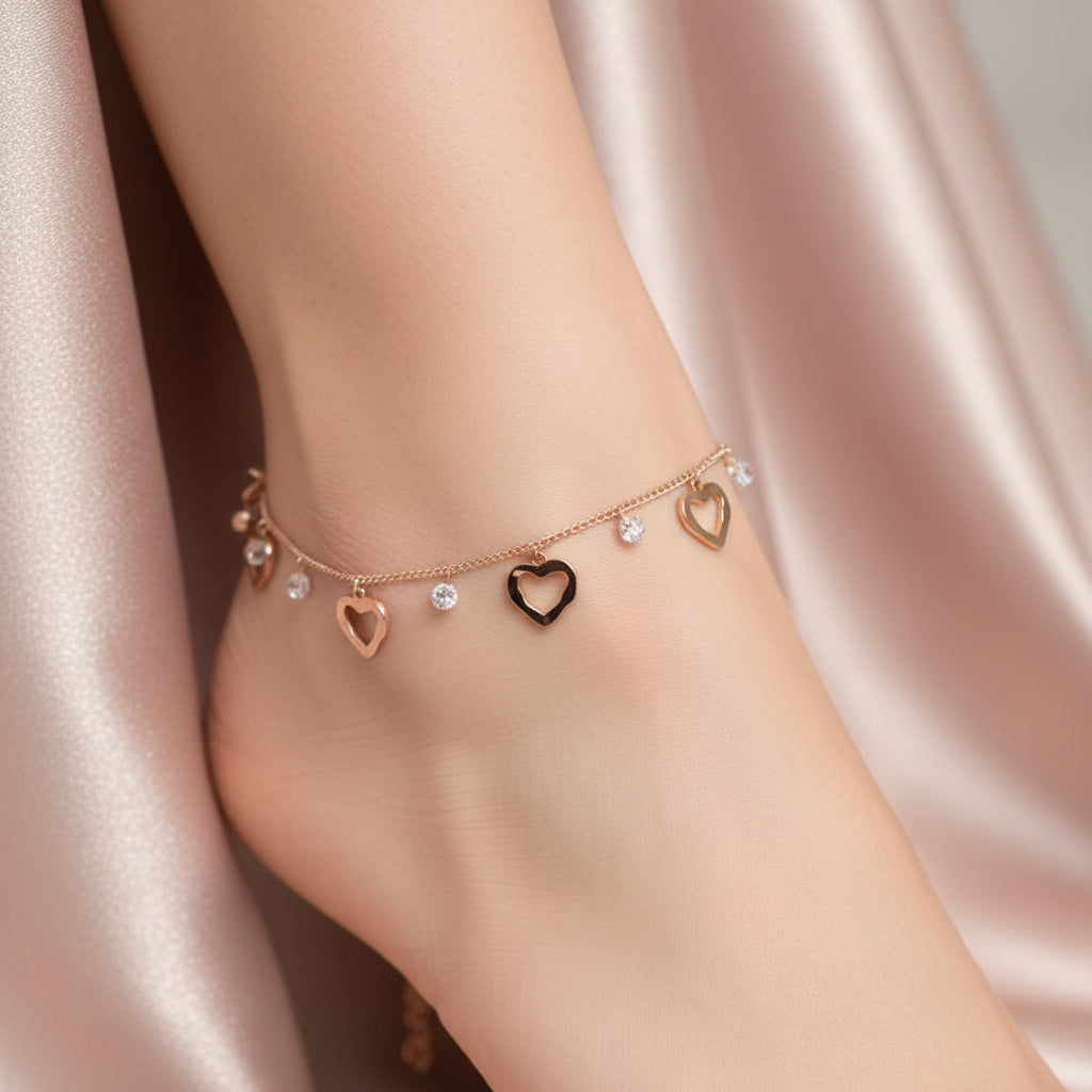 Gold anklet with heart-shaped charms on a dark background, featuring the brand 'Saheli'.