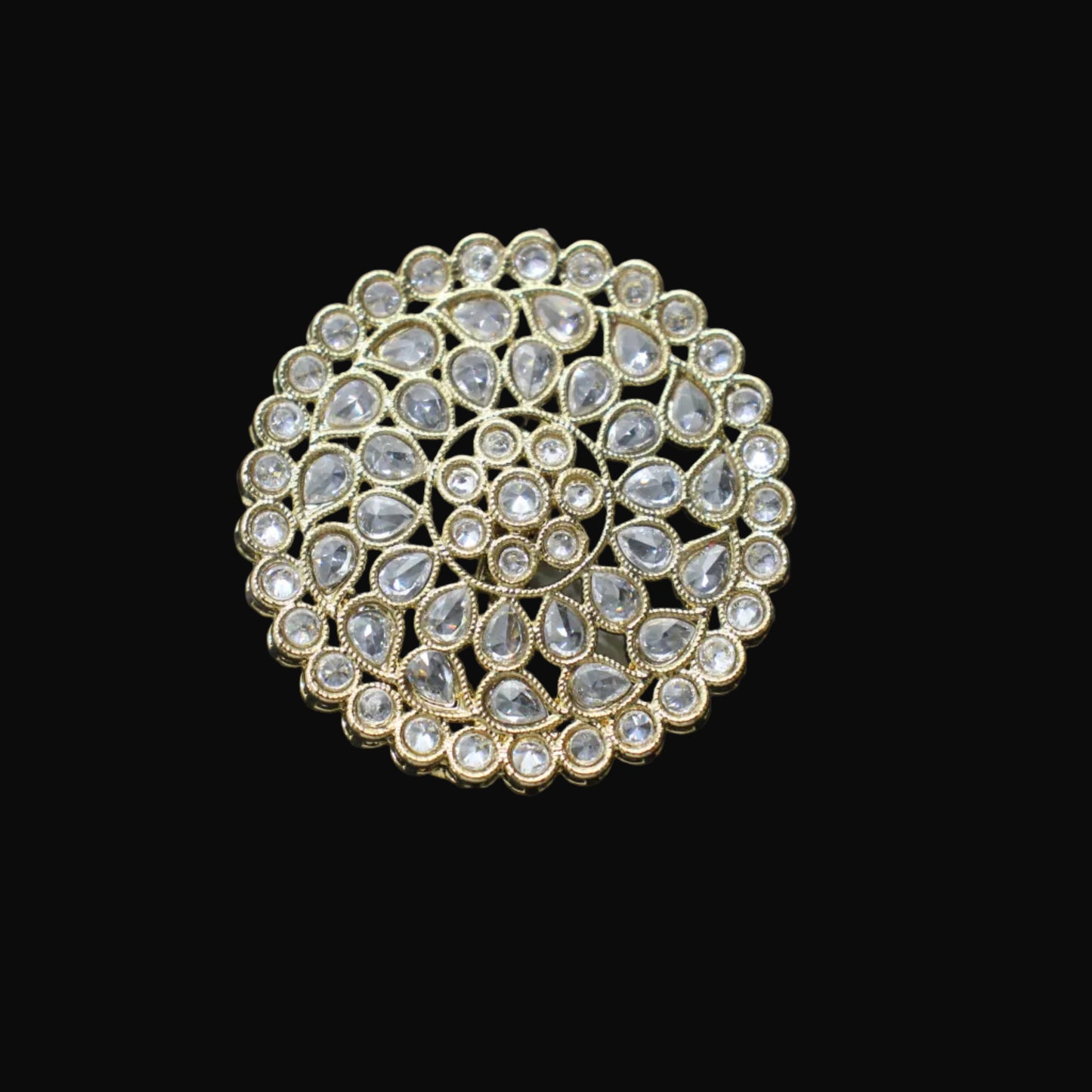 Gold and crystal brooch on a black mannequin hand against a dark background