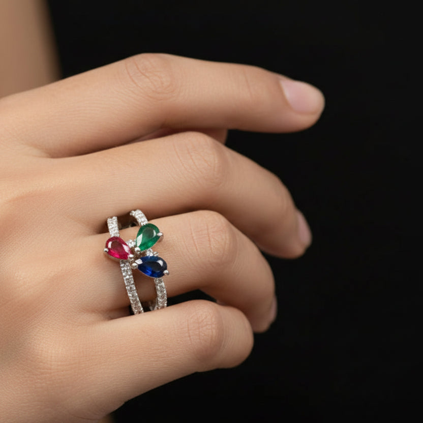 Jewelry ring with colored stones on a black background, featuring the brand 'Saheli'.