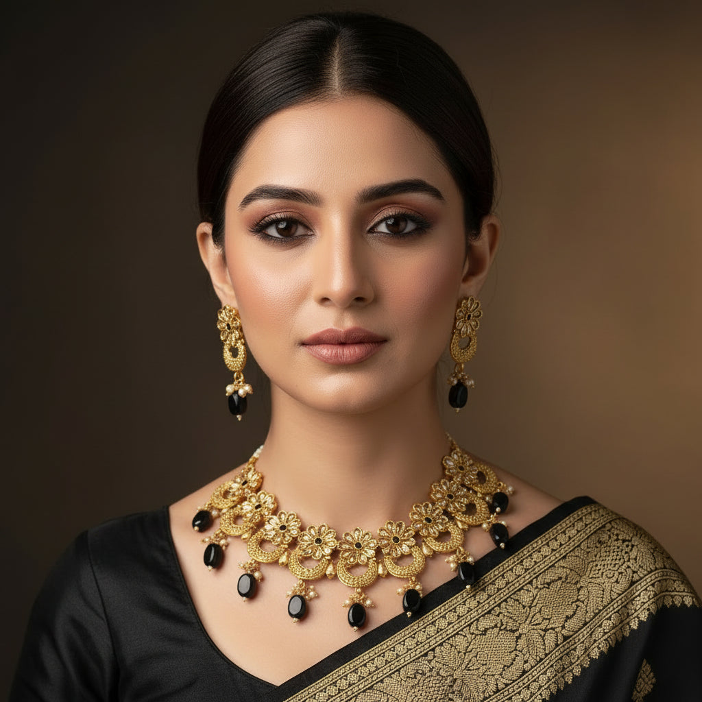 Gold necklace and earrings with black stones on a dark background, branded 'Saheli'.