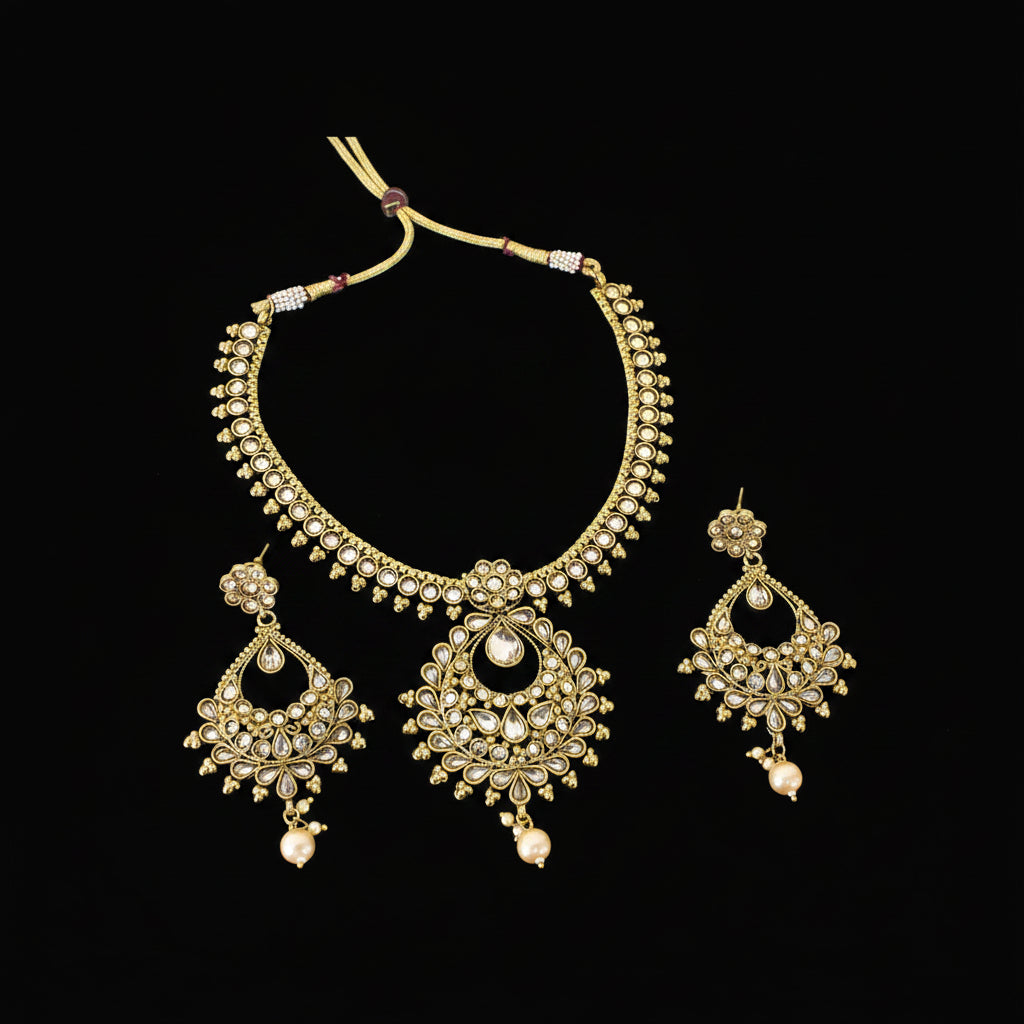 Gold-plated Indian traditional jewelry set featuring a necklace and matching earrings with intricate filigree work and small pearl-like accents, displayed on a dark gray reflective surface with the brand name 'SAHELI' visible in the center.
