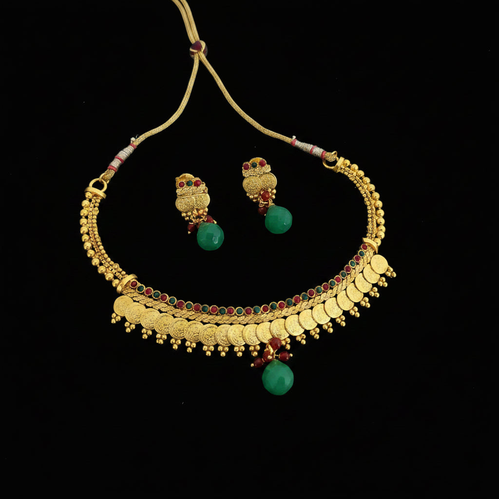 Gold-toned traditional necklace and matching earrings with green bead drops and red stone accents, displayed on a dark gray surface. The brand name SAHELI MY BEST FRIEND is visible in the top left corner.