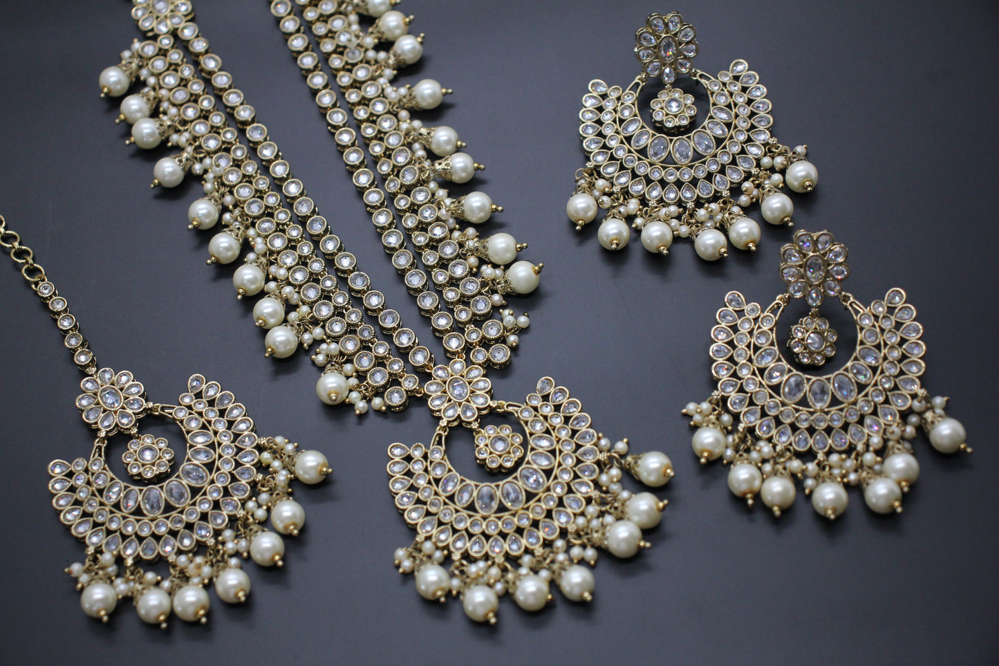 Ornate necklace and earrings with pearls and crystals on a dark background