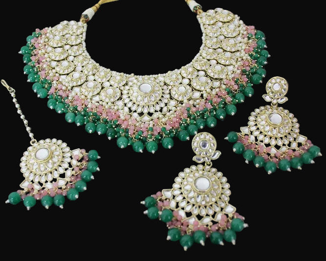 Ornate necklace and earrings set with green and pink stones on a dark background