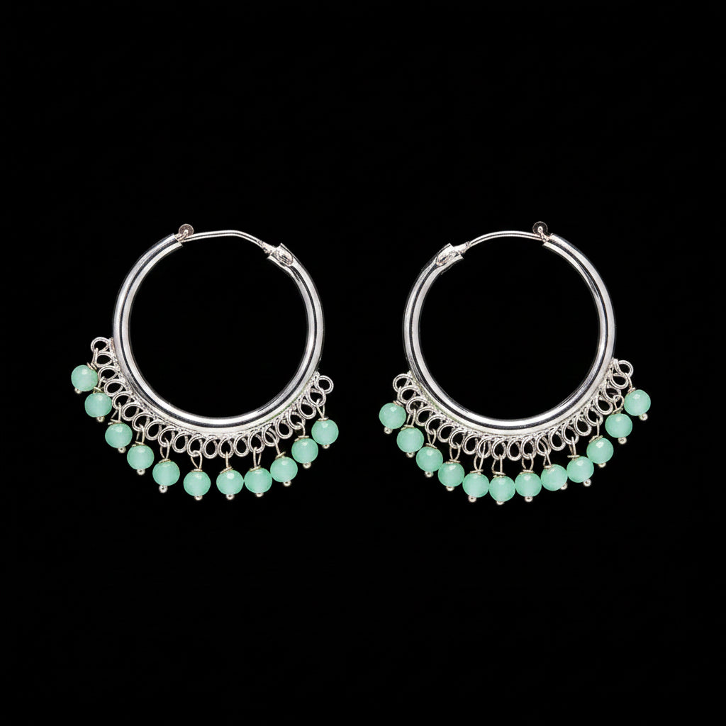 Silver hoop earrings with green beads on a brown background