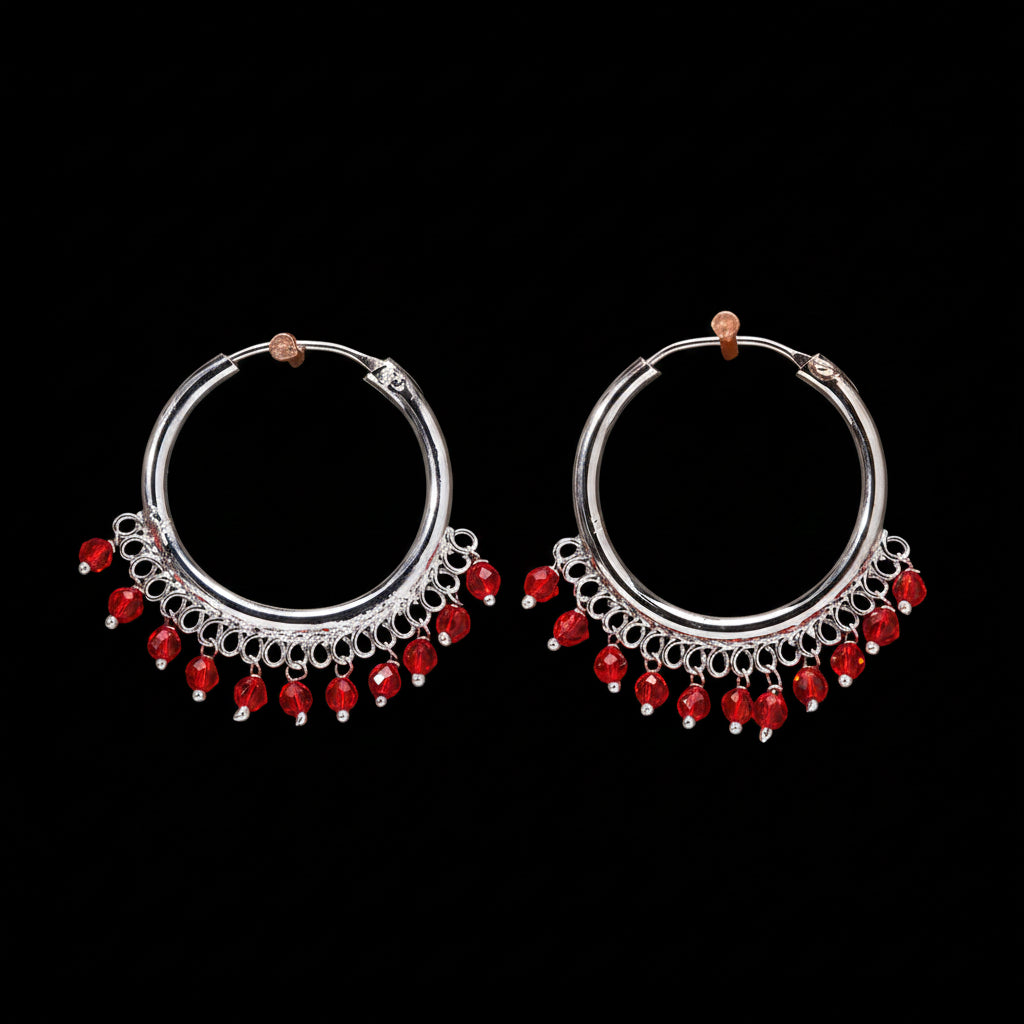 Pair of silver hoop earrings with red beads on a brown background